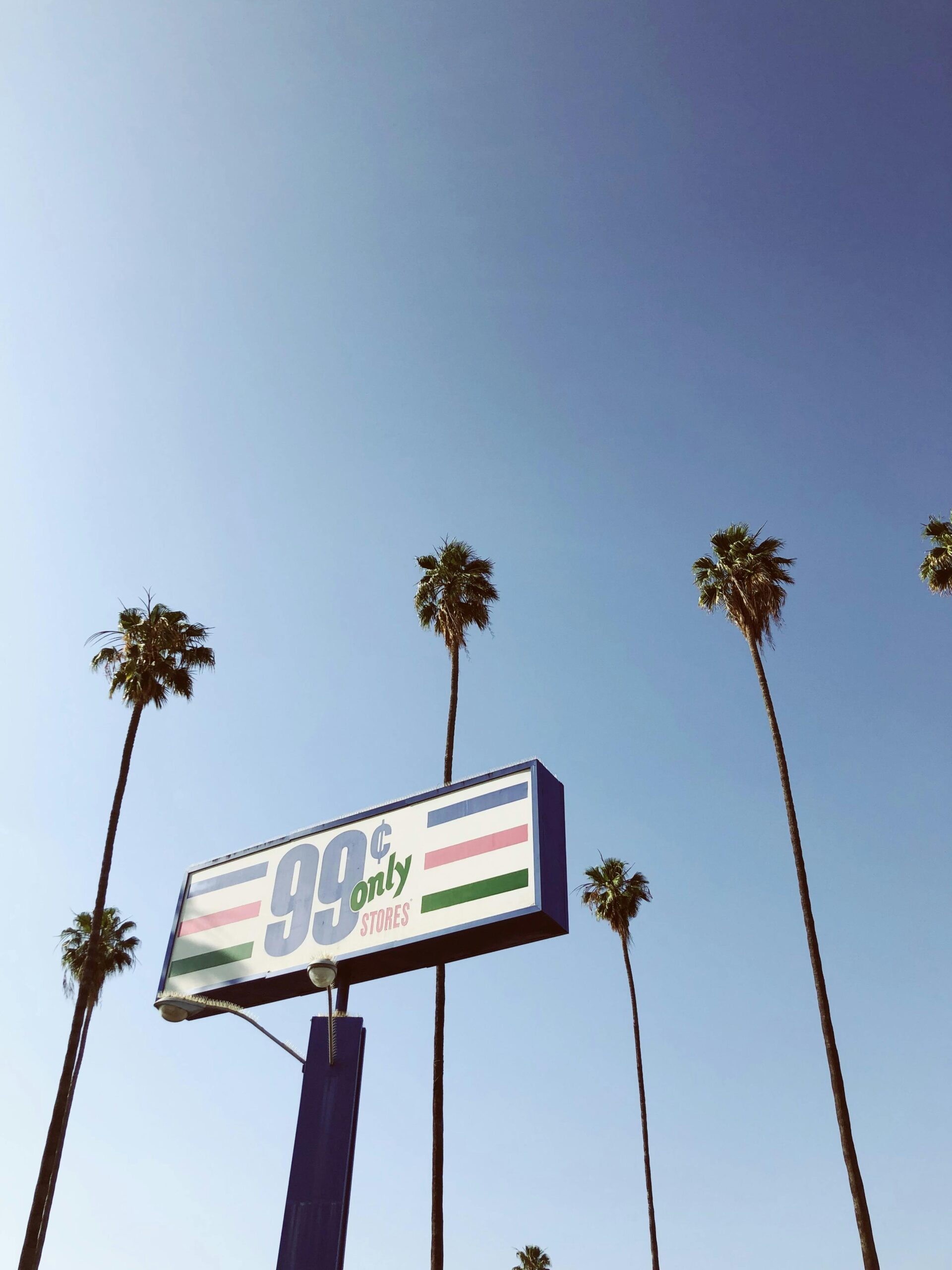 99 Cents Only Store sign under a clear blue sky with tall palm trees.